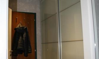 A bright hallway with a mirror and a wooden front door. A black jacket is hanging on the wall.