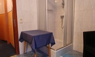 A small bathroom with a shower and a blue table. The floor is covered with colorful rugs.