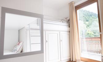 A modern bedroom with a high bed and plenty of natural light. Large windows offer a view of the greenery.
