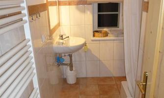 A small bathroom with a sink, a toilet, and a window. The walls are tiled and the floor is tiled.