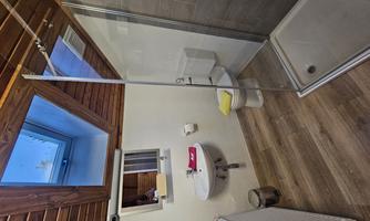 A modern bathroom with a shower and a window in the roof. There is a toilet, a sink, and wooden details on the ceiling.