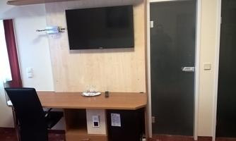 A simple room with a desk, a television, and a chair. In the background, there is a glass door leading to another room.