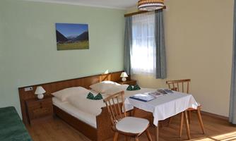 A cozy bedroom with two beds and a table. The room has large windows and is simply but beautifully furnished.