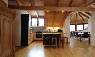 A modern kitchen with wooden shelves and a central cooking island. Bright windows and an open roof create a friendly atmosphere.