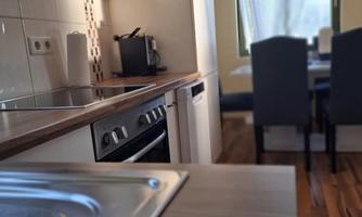 A modern kitchen with wooden surfaces and a dining area in the background. Plenty of light comes in through the window, creating an inviting atmosphere.