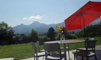A beautiful view of the mountains with a terrace. A red sun umbrella and a table with chairs are visible.