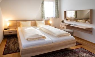 A cozy bedroom with a double bed, two pillows, and a modern decor. The room has a window with curtains and a stylish wall mirror.