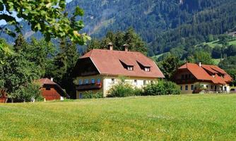 A picturesque landscape with green meadows and typical alpine houses. In the background, gentle mountains can be seen.