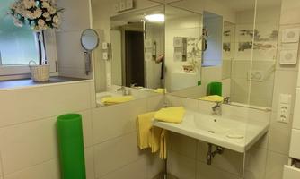 A modern bathroom with a sink and a large mirror. Yellow towels and a plant arrangement create a pleasant atmosphere.