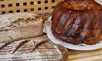 Three different breads are lying on a wooden board. There is also a braided cake on a white plate.