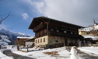 A charming wooden house in the snow with mountains in the background. In front of the house stands a snowman.