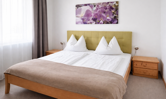 A modern bedroom with a double bed and two pillows. 

On the wall hangs a picture of purple flowers.