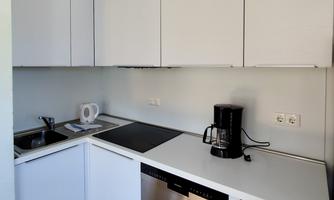 A modern kitchen with white cabinets and a bright design. Featured are a stovetop, a coffee machine, and a dishwasher.