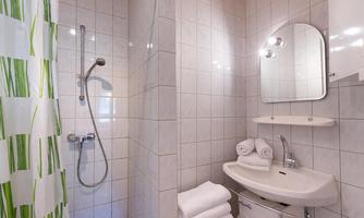 A modern bathroom with a shower cabin and a sink. The walls are tiled with light-colored tiles, and fresh towels are ready.