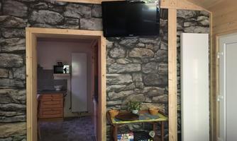 A cozy room with a stone wall and a television. In the background, a small kitchen is visible.