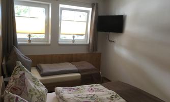 A bright bedroom with two beds and colorful pillows. There are two windows and a television on the wall.