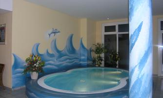 An elegant wellness area with a round jacuzzi and a mural of waves. The plant decoration creates a relaxed atmosphere.