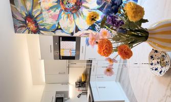 A modern kitchen with white cabinets and a colorful flower pattern on the wall. On the table stands a vase with colorful flowers.
