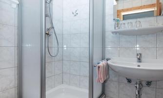 A modern bathroom with a shower cabin and a sink. The walls are tiled and there is a wood ceiling accent.