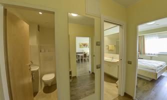 A bright hallway with two doors leading to a bathroom and a bedroom. The floor is made of wood and the walls are painted in a soft shade of yellow.