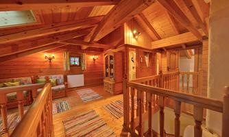 A cozy wooden room with wood paneling and an open upper floor. The room is furnished with carpets and a small seating area.