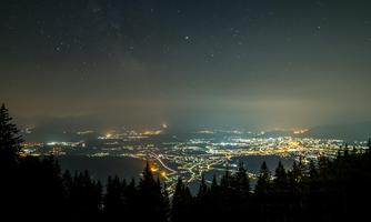 A nighttime landscape with sparkling city lights in the valley. The sky is dark and the stars are visible.