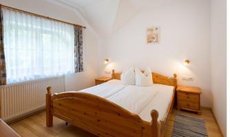 A cozy bedroom with a wooden double bed and two nightstands. The bright window front ensures plenty of daylight.