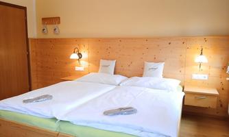 A cozy bedroom with a large double bed and wooden decor. Soft lighting creates an inviting atmosphere.