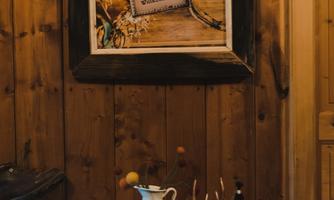 A cozy room with wooden walls. On a table, there are slippers, a bottle, and a vase with flowers, while a picture hangs on the wall.