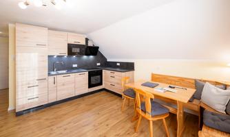 A modern kitchen with wooden cabinets and a dining table. The space is designed to be bright and welcoming.