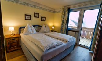 A cozy bedroom with two beds and soft lighting. There is access to a balcony with a view of the surroundings.