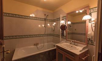 A bathroom with a bathtub and a sink. The walls are decorated with white tiles and a green pattern.
