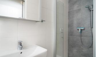 A modern bathroom with a clear shower cabin and a white sink. The walls are brightly tiled, and a mirror hangs above the sink.