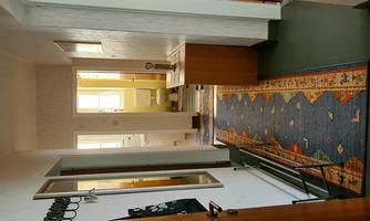 A bright hallway with a colorful carpet and a small wooden cabinet. In the background, a bathroom is visible.
