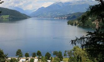A picturesque lake surrounded by mountains and trees. Campsites are visible in the foreground.