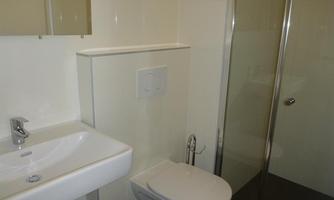 A modern bathroom with a sink, toilet, and shower. The walls are bright and the fixtures are simple and functional.