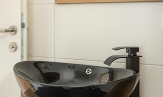 An elegant black sink stands on a wooden panel. In the background, there is a mirror with a wooden frame.