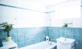 A modern bathroom with blue tiles and plenty of natural light. The bathtub and the sink are functionally and stylishly furnished.