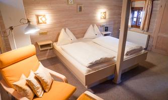 A cozy bedroom with two single beds and an orange armchair. Wooden paneling and warm lighting create an inviting atmosphere.