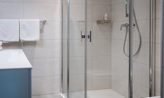 A modern bathroom with a glass door shower and a sink. The walls are brightly tiled and there are fresh towels.