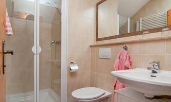 A modern bathroom with a shower, a toilet, and a sink. Towels in soft shades are hung up.