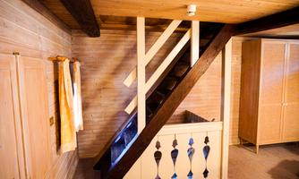 A cozy room with a wooden staircase and light walls. In the background, there is a wooden wardrobe.
