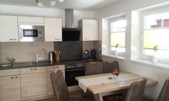 A modern kitchen with a dining area. There are bright furniture and large windows that let in a lot of light.