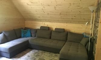 A cozy living room with a large, gray couch and wooden paneling. The light gently falls through the skylight.