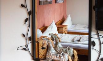 A mirror with a decorative frame reflects a cozy room with wooden beds and pictures on the wall. In front of the mirror stands a small decorative horse statue.