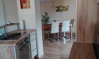 A modern kitchen with wooden details and a cooktop. In the background, there is a dining area with a table and chairs.