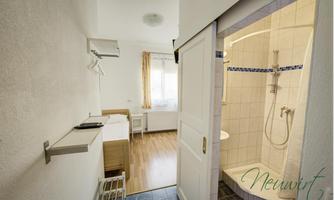 A simple room with a bathroom and a modern shower. There is a desk and plenty of natural light through the window.