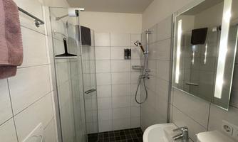 A modern bathroom with a walk-in shower and a sink. The walls are brightly tiled, and there is a large mirror.