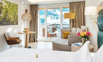 A modern hotel room with a comfortable sofa and a table. Large windows offer a view of the mountains and the balcony.