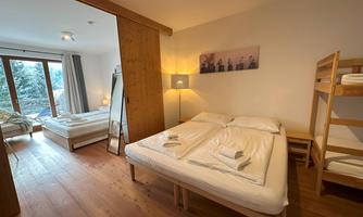 A cozy bedroom with a large bed and a bunk bed. Large windows provide plenty of daylight and a view outside.